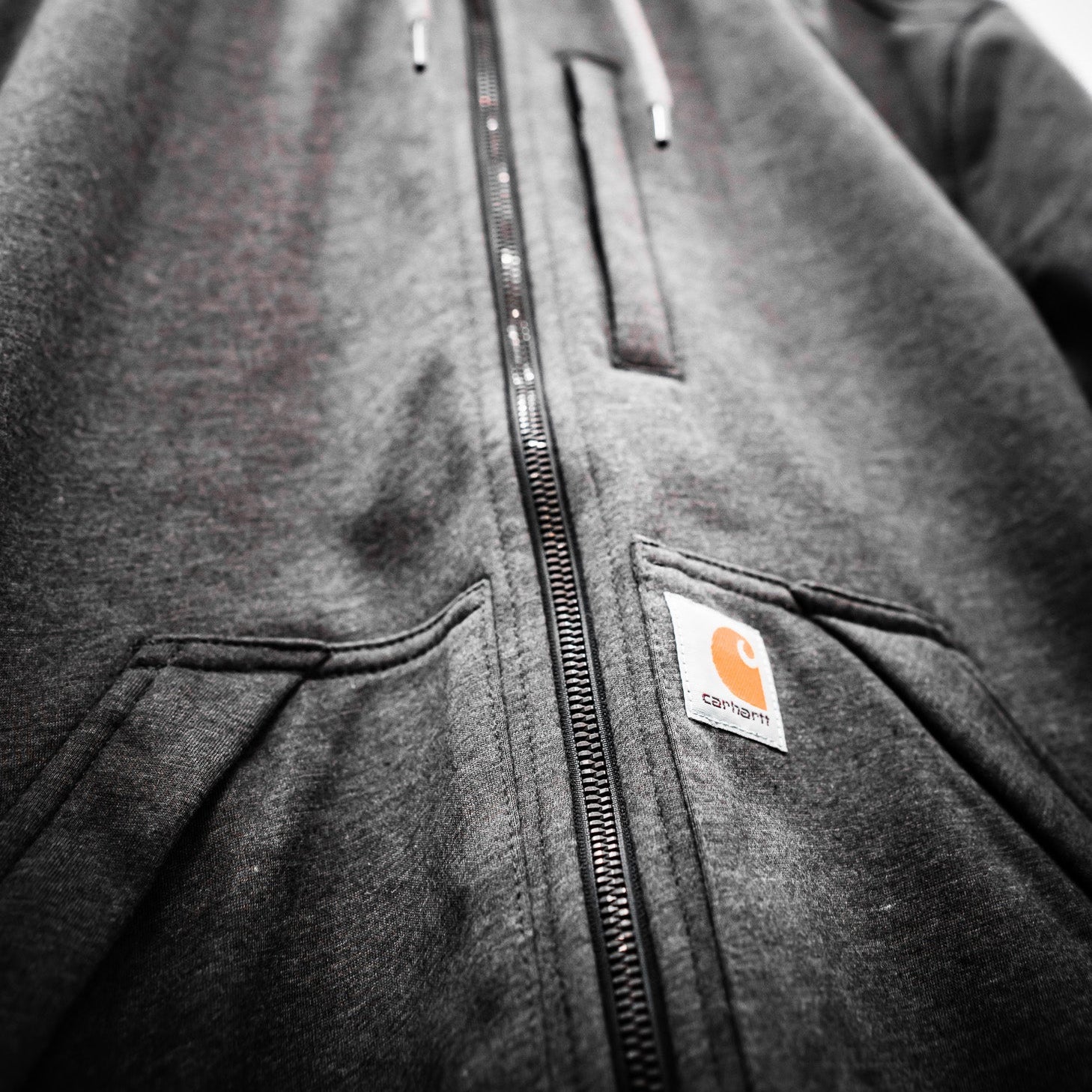 Close-up of a gray hoodie with a visible brand logo on a light background
